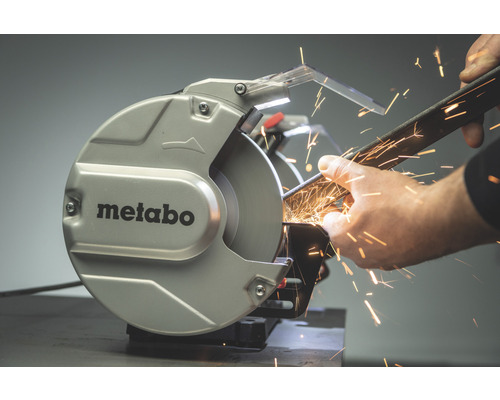 Metabo Logo. Eine Person schleift ein Metallstück mit einer Schleifmaschine, wobei Funken entstehen.