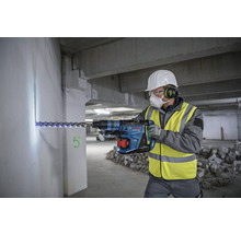 Handwerker bohrt mit einem Bohrhammer in eine Wand. Der Bohrhammer ist blau.