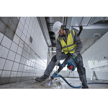 Ein Arbeiter in Schutzkleidung benutzt einen Abbruchhammer in einem gefliesten Raum.