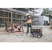 Mann schneidet Armierungseisen mit einem Trennschleifer auf einer Baustelle. Im Hintergrund ist ein Stromgenerator zu sehen.