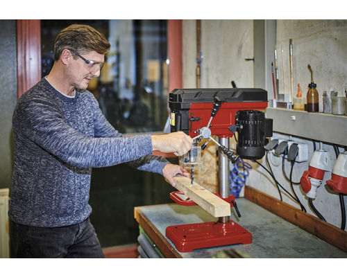 Mann bohrt mit einer Tischbohrmaschine ein Holzbrett