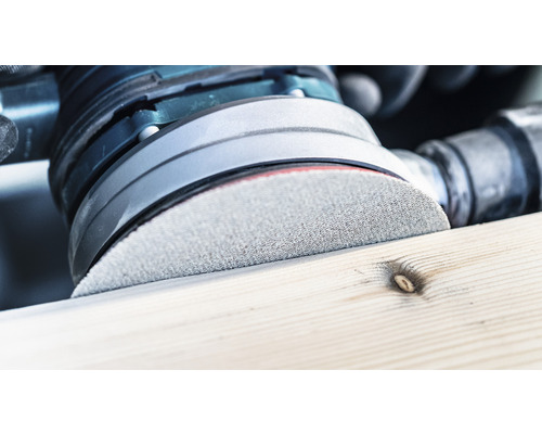 Detailaufnahme eines Schleifgeräts beim Bearbeiten eines Holzstücks.