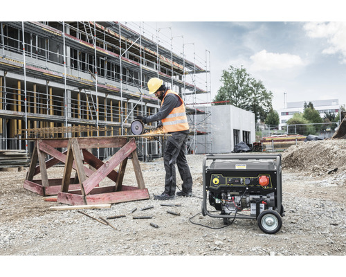 Ein Bauarbeiter schneidet mit einem Trennschleifer Stahlträger auf einer Baustelle, ein Kärcher Stromerzeuger steht im Vordergrund.