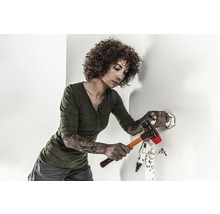 Eine Frau hämmert mit einem Hammer auf einen Dübel an einer Wand.