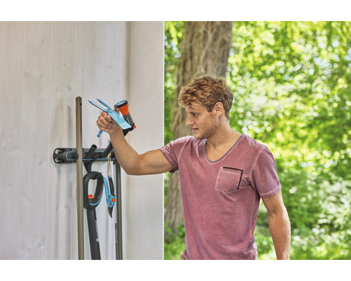 Mann ordnet Gartengeräte an einer Gerätehalterung an der Wand an