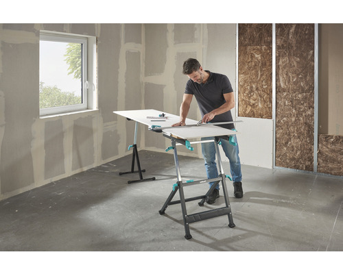 Mann schneidet Gipskartonplatte auf einem Wolfcraft Arbeitstisch in einem Rohbau.