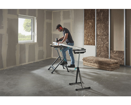 Ein Mann arbeitet mit einer Stichsäge an einem Werkstück auf einer Wolfcraft Werkbank in einem Raum mit Gipskartonplatten und Dämmmaterial.