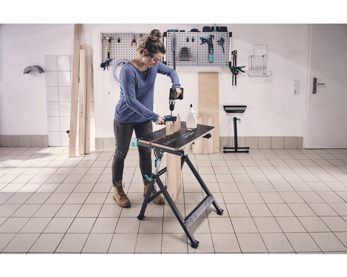 Frau arbeitet mit Bohrmaschine an einer Werkbank in einer Werkstatt.