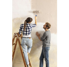 Frau streicht Wand mit Farbroller, Mann schaut zu.