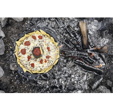 Eine gusseiserne Pfanne mit Nachos, Käse, Hackfleisch und Salsa über einem Lagerfeuer.