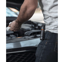 Eine Person wischt mit einem Tuch unter der Motorhaube eines Autos, während eine Taschenlampe an ihrer Hose befestigt ist.