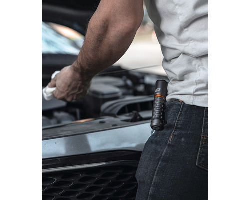 Eine Person wischt mit einem Tuch unter der Motorhaube eines Autos, während eine Taschenlampe an ihrer Hose befestigt ist.