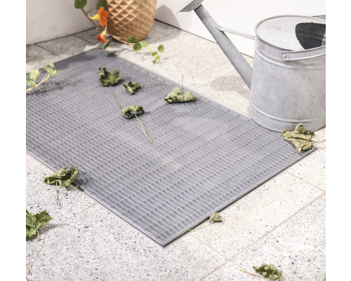 Grauer Fußabtreter aus Gitterstruktur mit Blumenvase und Gießkanne