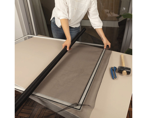 Person installiert ein Fliegengitter in einen Rahmen mit Werkzeugen auf einem Tisch.