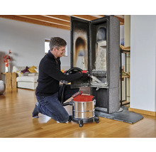 Ein Mann reinigt einen Kaminofen mit einem Aschesauger in einem Wohnzimmer.