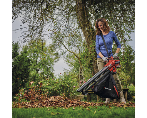 Frau benutzt einen Laubsauger im Garten, um Laub zu entfernen.