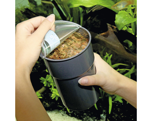 Eine Person öffnet eine Dose Fischfutter vor einem Aquarium