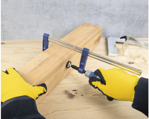 Anziehen einer Schraubzwinge an einem Holzbrett mit Handschuhen