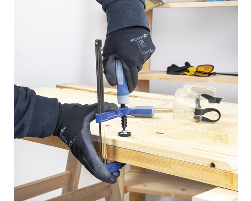 Eine Person fixiert ein Holzbrett mit einer Schraubzwinge.