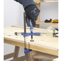 Eine Person befestigt ein Werkstück mit einer Schraubzwinge auf einer Holzoberfläche.