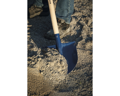 Eine Schaufel mit einem Holzgriff und einer Person, die in Arbeitskleidung Sand schaufelt