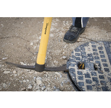 Spitzhacke mit Holzstiel neben Kanaldeckel