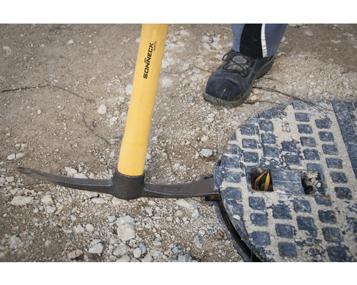 Spitzhacke mit Holzstiel neben Kanaldeckel
