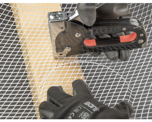 Eine Person befestigt Drahtgeflecht mit einem Tacker an einem Holzrahmen.