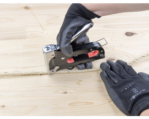 Person befestigt Seil mit einem Tacker auf Holz