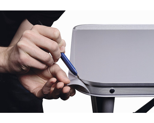 Eine Person schneidet mit einem Bastelmesser eine Folie auf einer Oberfläche zu.