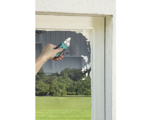 Handwerker entfernt mit einem Schaber alte Farbe von einem Fensterrahmen.