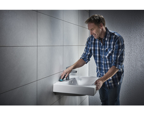 Mann reinigt ein Waschbecken im Badezimmer mit einem Reinigungswerkzeug