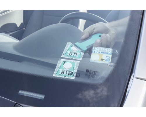 Eine Hand entfernt mit einem Schaber Aufkleber von einer Windschutzscheibe.