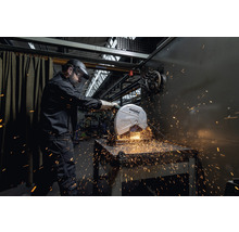 Mann mit Schutzhelm und Schutzbrille bedient eine Metabo-Trennmaschine beim Schneiden von Metall, Funken fliegen.