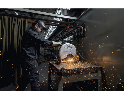Mann mit Schutzhelm und Schutzbrille bedient eine Metabo-Trennmaschine beim Schneiden von Metall, Funken fliegen.