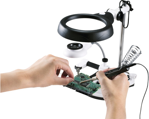 Person lötet Platine mit Lötkolben unter Lupe