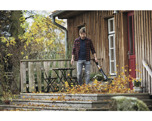 Mann benutzt einen Laubsauger auf einer Holzterrasse, um Laub zu entfernen.