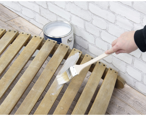 Anstreichen einer Holzlattenkonstruktion mit einem Pinsel neben einem Farbeimer