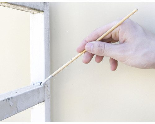 Hand streicht mit Pinsel ein Metallgitter