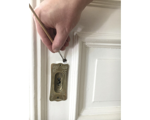 Anstreichen einer weißen Tür mit einem Pinsel in der Nähe eines Schlüssellochs