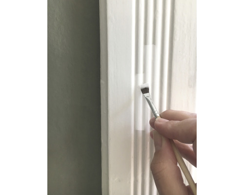 Eine Person streicht eine weiße Zierleiste mit einem Pinsel.