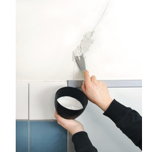 Eine Person verschließt mit einem Spachtel einen Riss in der Wand. Eine Schale mit Füllmaterial wird gehalten.