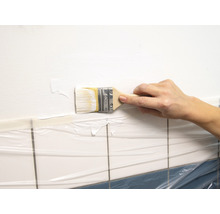 Eine Hand streicht mit einem Pinsel eine Wand in einem Badezimmer.
