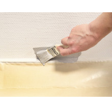 Eine Person streicht mit einem Pinsel eine Wand entlang einer Abdeckbandlinie.