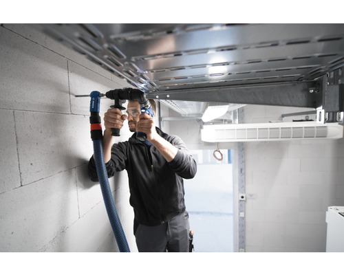 Mann bohrt Loch in Wand mit Bohrhammer und Absaugvorrichtung