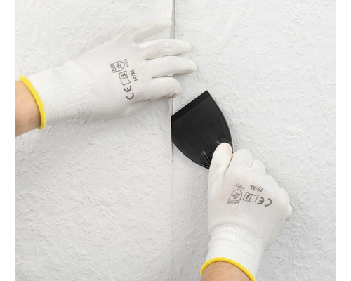 Person glättet Tapete mit Spachtel und Schutzhandschuhen