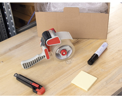 Karton, Klebebandabroller, Markierstift, Notizzettel und Teppichmesser auf einem Tisch.