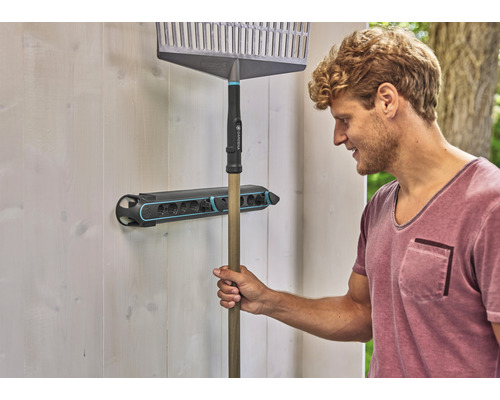 Mann hängt einen Rechen in eine Gerätehalterung an einer Wand