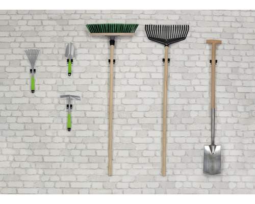 Gartengeräte wie Besen, Rechen, Schaufel und Hacke hängen an einer Wand