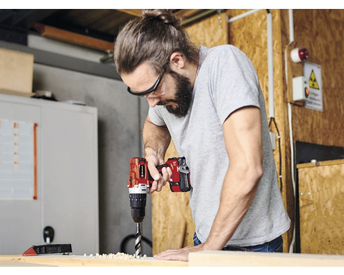 Mann bohrt mit einer Bohrmaschine in ein Holzbrett